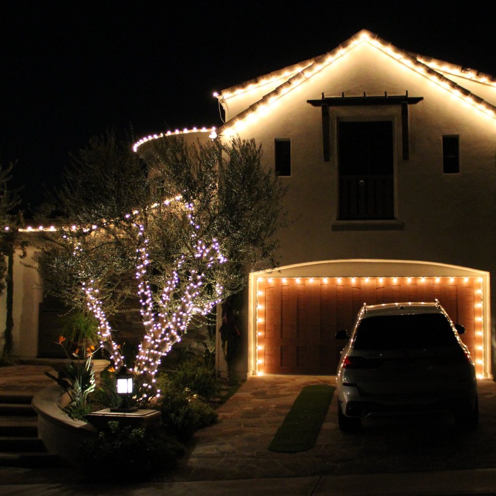 Home with warm white Christmas lights along the roofline, garage and tree