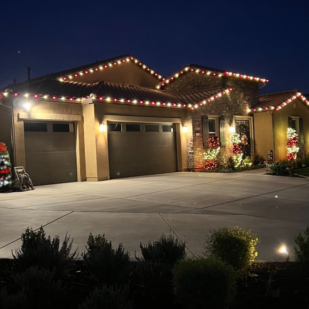Red and white Christmas lights on a tile roof with lit wreath trees